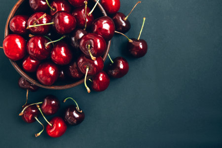 Close-up of red ripe cherries in a wooden bowl on a dark background. Summer background with copy spaceの写真素材