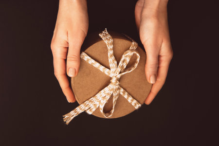 Craft gift box with beige rope in woman's hands on a dark backgroundの写真素材