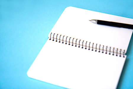 Open spiral notebook with blank white pages and pen on blue background. Side viewの写真素材