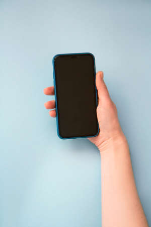 Woman's hand holding and smart phone on a light blue background. Mock upの写真素材
