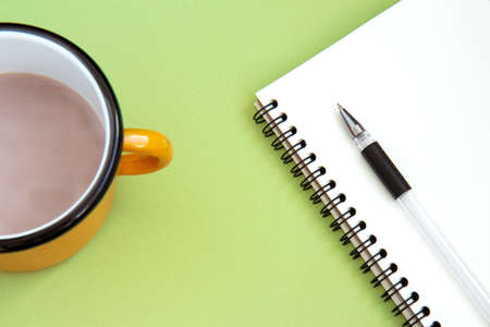 Open white notebook with blank white pages, pen and iron orange cup with cocoa on green background. Flat layの写真素材