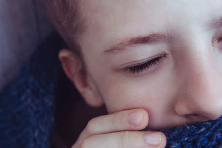 Beautiful girl with closed eyes wrapped herself in a warm blue knitted sweater