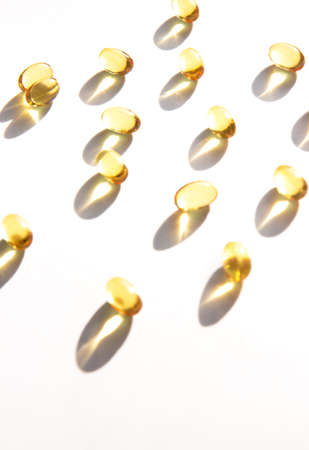 Shiny yellow fish oil capsules isolated on a white background with shadows of focus on the table. Vitamin E. Copy space for your textの写真素材