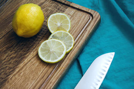 Lemon and slices of yellow lemon lie on a wooden cutting board and knife on a background of turquoise fabric. Tropical fruits. Fresh citrus. Free space for text. Top viewの写真素材