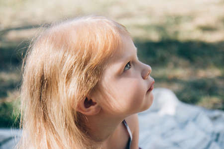 Cute little girl in a summer plaid sundress. Child sitting on a light blanketの写真素材