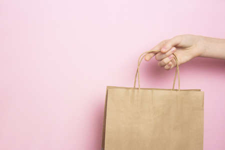 Girl holding in hand beige craft paper bag for shopping on pink background. Shopping conceptの写真素材