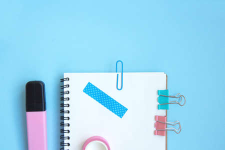 White open notebook with paper clip, clip and piece of scotch tape on blue background. Set...