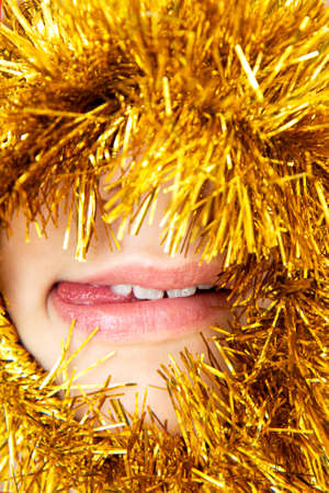 Face of a beautiful young girl with sticking out tongue peeking out from bright yellow garlandの写真素材