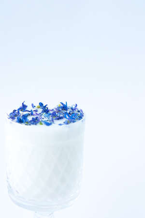 Beautiful crystal glass with milk and blue flower petals on a white background. Abstract background. Floral pattern of blue flower petals on white backgroundの写真素材