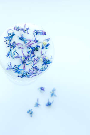 Beautiful crystal glass with milk and blue flower petals on a light background. Abstract background. Floral pattern of blue flower petals on white backgroundの写真素材