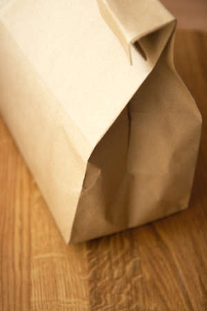 Brown craft paper bag on light wooden background. Recycled paper shopping bag, lunch bagの写真素材