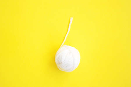 One white ball of woolen thread with long twisted thread on yellow background with copy spaceの写真素材