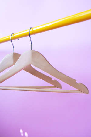 Two wooden clothes hangers hang on a yellow rack on a violet background