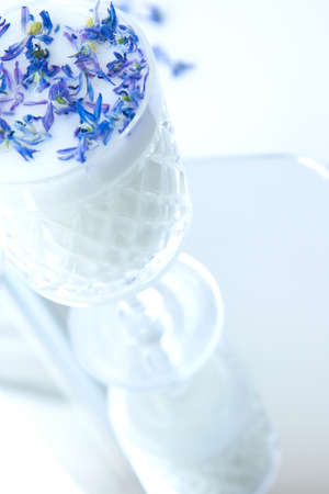 Beautiful crystal glass with milk and blue flower petals standing on the mirror. Flowers in milkの写真素材