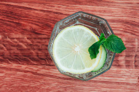 Lemon slice in a glass of sparkling water with mint leaves on a red wooden background. Refreshing summer drink. Fresh citrus. Free space for text. Top viewの写真素材