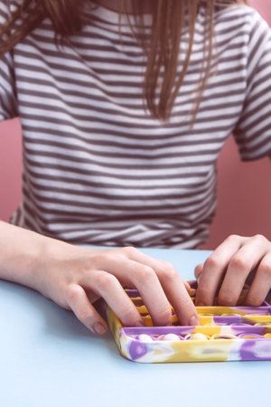 Child in casual clothes plays with trend bright multicolored antistress toy Pop. Poppit new fidget toy on empty pink background. Close upの写真素材