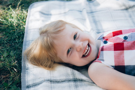 Cute little girl in a summer plaid sundress. Child lies on a light blanket on the grassの写真素材