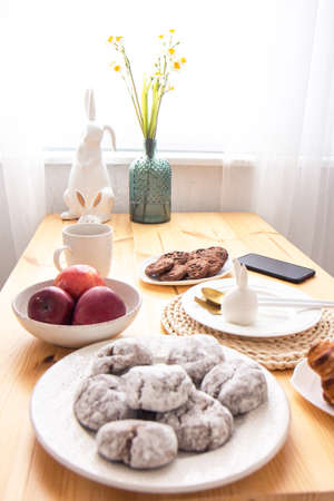 Narcissus flowers in a beautiful vase, chocolate cookies on a plate and red apples on a wooden table...