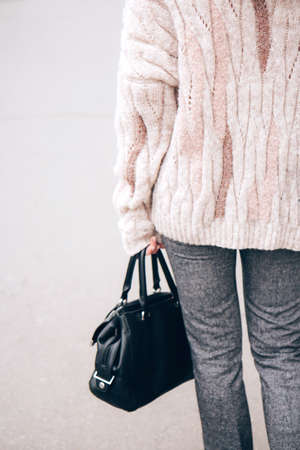 Young beautiful woman in a cozy nude cardigan and a black handbag spends time outdoors. Lifestyle....