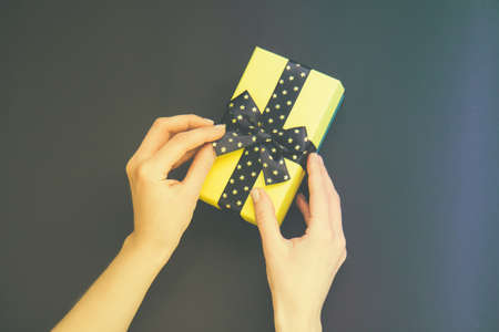 Yellow gift box with black bow with golden stars in woman's hands on a dark backgroundの写真素材