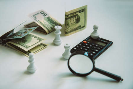 Magnifier, calculator, paper money and white chess isolated on light background in vintage retro style. Concept of debt management, payment of taxes and investingの写真素材