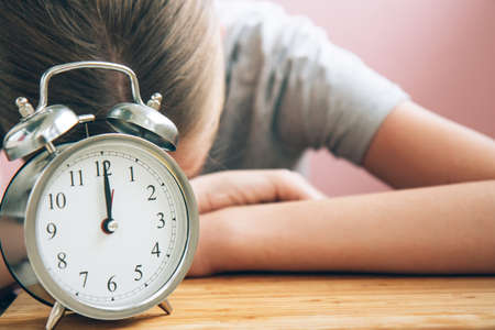 Tired student with retro alarm clock preparing for exams on bright light pink background with copy...