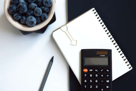 Notepad with white and black paper, calculator, pen and blueberries isolated on white backgroundの写真素材