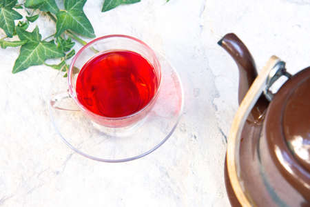 Glass cup of hot red hibiscus tea and old retro teapot on tray