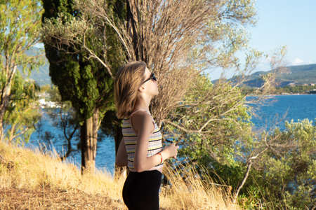 Young beautiful teenage girl stands on the seashore and enjoys the landscapeの写真素材