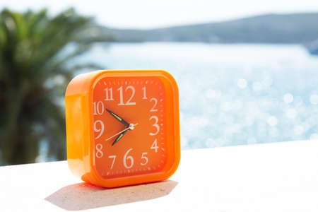 Orange alarm clock in a rays of sun on the background of the seascapeの写真素材