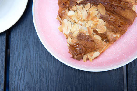 Delicious and tasty croissants with slices nuts in pink plate on black wood background. Flat layの写真素材