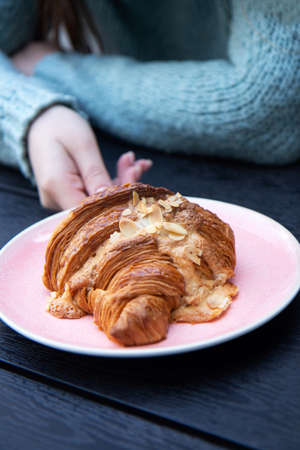 Delicious and tasty croissants with slices nuts in pink plate on black wood background and female...