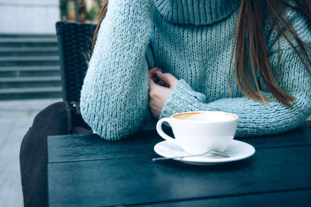 Woman in a cozy blue sweater drinking coffee in a street cafeの写真素材