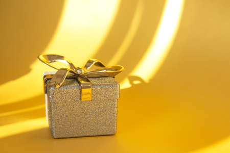 Shiny silver gift box with golden bow on bright gold background. Holiday conceptの写真素材