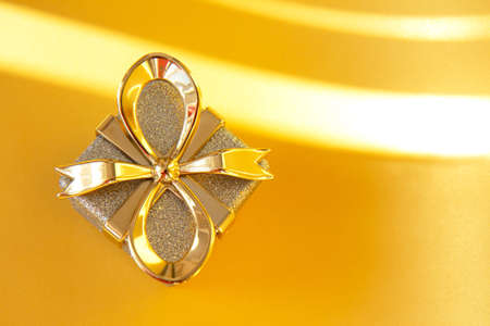 Shiny silver gift box with golden bow on bright gold background. Holiday concept. Top viewの写真素材