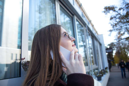 Woman with long hair in a dark coat walks down the street and talking on a mobile phoneの写真素材