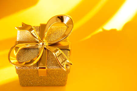 Shiny silver gift box with golden bow on bright gold background. Holiday concept with copy spaceの写真素材
