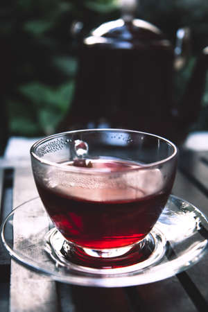 Glass cup of hot red hibiscus tea on a wooden tray at terrace. Close up