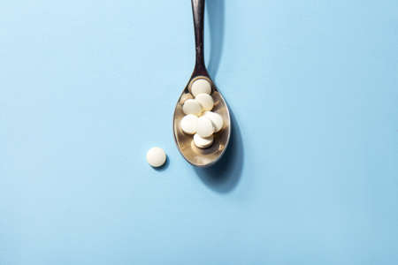 Dietary supplements. Vitamin tablets in an iron spoon on a blue background. Complementary and...