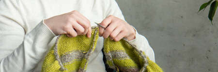 Young woman knitting warm colorful sweater at home. Concept of needlework. close up. Bannerの写真素材