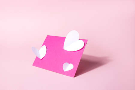 Pink envelope with white paper hearts on nude pink background. White volumetric paper hearts....