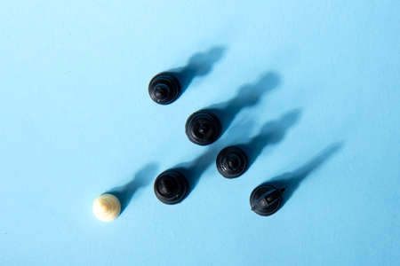 One chess piece against black chess pieces on a blue background with contrasting shadows. abstract...