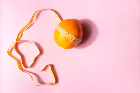 Bright yellow measuring tape wrapped around an orange isolated on a pink background with copy spaceの写真素材