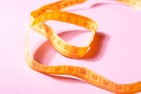 Bright yellow measuring tape isolated on a pink background. close upの写真素材