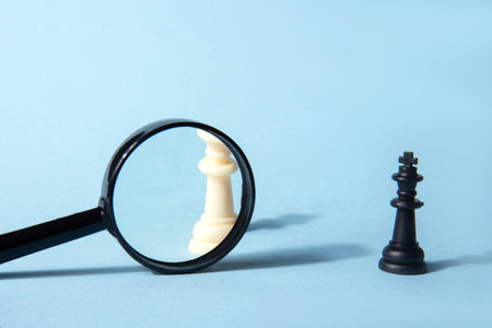 White chess queen, black chess queen and magnifying glass on a blue background. abstract background. H.R. Concept of search for new employeesの写真素材