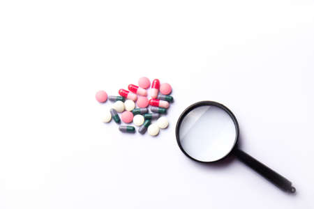 Vitamin tablets and a magnifying glass on a white background. dietary supplements and pills for dieting. medical concept. Complementary and medical productsの写真素材