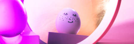 Easter holiday concept with cute handmade egg. Cute face egg looks in the mirror on a pink background with neon light. Bannerの写真素材