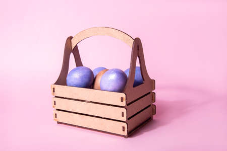 Wooden craft basket with purple painted shiny Easter eggs on a pink background. easter holiday conceptの写真素材