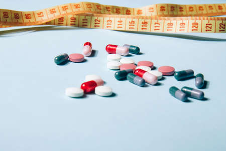 Vitamin tablets and capsules and bright yellow measuring tape on a blue background. Dietary supplementsの写真素材