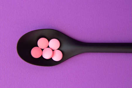 Dietary supplements. Vitamin tablets on black spoon on a violet backgroundの写真素材